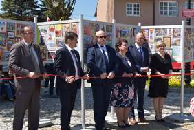 6 osób (2 kobiety, 4 mężczyzn) na tle wystawy trzyma w ręku pomarańczowa wstęgę, którą będą przecinać