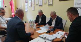 Pokaż zdjęcie: pomieszczenie w siedzibie Oddziału, po środku stoi duży owalny stół przy którym siedzi 5 mężczyzna , na stole dokumenty które podpisują osoby upoważnione 