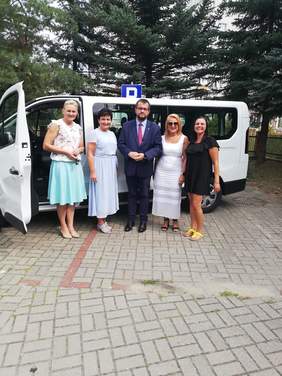 Pokaż zdjęcie: Osoby przekazujące busa stoją obok siebie na tle auta na podwórku