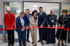 Pokaż zdjęcie: Elegancko ubrani kobiety i mężczyźni przecinają czerwoną, szeroką wstęgę w pomieszczeniu szpitala.. 