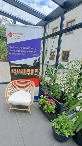 Ogród zimowy, a w tle baner reklamujący budowę ośrodka