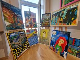 Pokaż zdjęcie: Cztery drewniane sztalugi, na których ustawione są barwne obrazy