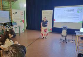 Pokaż zdjęcie: Kobieta prelegentka prowadzi wykład. Na ekranie slajd z prezentacji, po lewej stronie sali rollup z logo CIDON oraz OWiT.