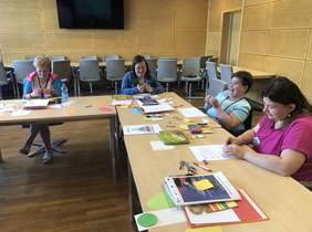 Pokaż zdjęcie: na zdjęciu: uczestnicy warsztatu siedzą przy biurkach i wykonują prace manualne zlecone przez trenera 