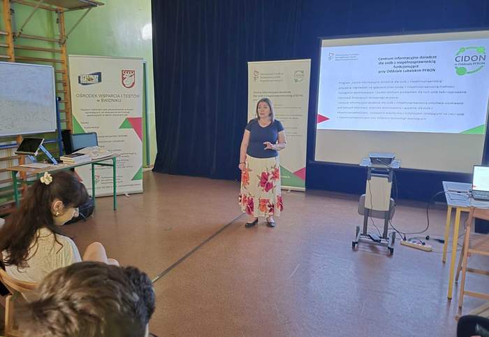 Pokaż zdjęcie: Kobieta prelegentka prowadzi wykład. Na ekranie slajd z prezentacji, po lewej stronie sali rollup z logo CIDON oraz OWiT.