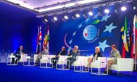 Scena, na niej na krzesłach siedzą paneliści