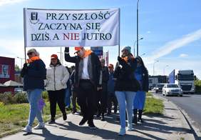 Pokaż zdjęcie: Ulicami Zgierza idą ludzie. Niosą transparent z hasłem: „Przyszłość zaczyna się dziś, a nie jutro”. W tle widać samochody i budynki.  