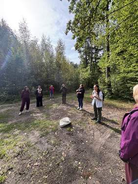 Pokaż zdjęcie: Grupa osób stoi na leśnej ścieżce wśród drzew. Uczestnicy są ustawieni w półokręgu.