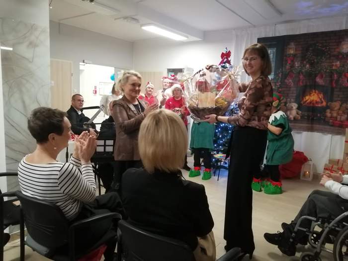 Pokaż zdjęcie: W pomieszczeniu placówki znajdują się uczestnicy jubileuszu i widoczną są wręczone upominki oraz osoby z niepełnosprawnościami w świątecznych przebraniach