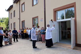 ksiądz poświęcający nowe pomieszczenia, on oraz inni zebrani, kilkanaście osób, stoją przed budynkiem zakładu
