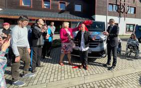 Pokaż zdjęcie: Dyrektor Marta Mordarska oraz zebranie goście podczas uroczystego przekazania pojazdu dla uczestników ŚDS w Krynicy-Zdroju. Radośni uczestnicy wydarzenia stoją przed samochodem