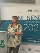 Osoba stojąca przy mównicy z napisem ZUS. W tle baner informujący o dniach seniora.
