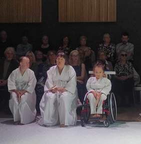 Pokaż zdjęcie: Scena w której aktorzy w białych szatach siedzą