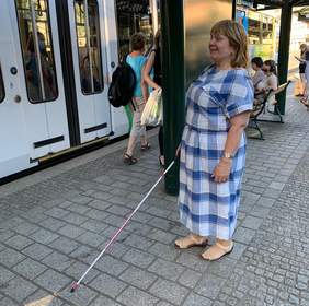 Pokaż zdjęcie: Na zdjęciu kobieta z białą laską na przystanku - trening orientacji w ramach kampanii "Widzialni (nie)widzialni"