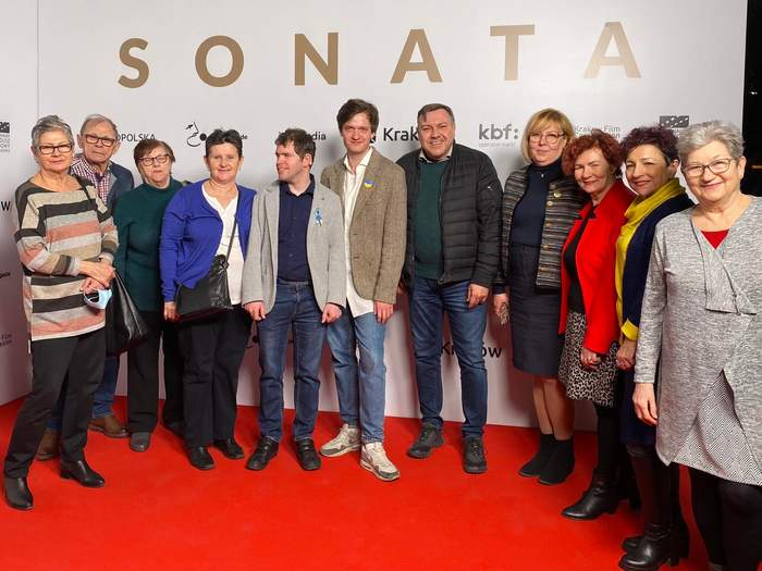 Pokaż zdjęcie: Liczna grupa kobiet i mężczyzn. Wszyscy stoją na czerwonym dywanie, w tle ścianka z napisem "Sonata"