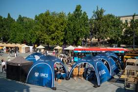 Pokaż zdjęcie: Zdjęcie placu na którym stoją namioty wystawców, przed namiotami spacerują odwiedzający targi.