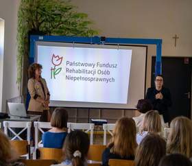 Prezentacja PFRON podczas spotkania „Spektrum Możliwości” w szkole w Lublinie; dwie osoby prowadzą wystąpienie przed uczestnikami, na ekranie widoczne logo PFRON.
