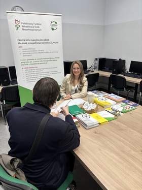 Widok z góry na uczestników Targów Pracy na Uniwersytecie Przyrodniczym w Poznaniu. W hali widać tłum osób rozmawiających przy stoiskach wystawienniczych, flagi oraz roll-upy promocyjne.