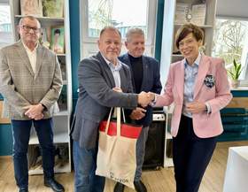 W centrum stoją dwie osoby: Michał Pawlak – kierownik placówki oraz Anna Skupień – dyrektor Oddziału Wielkopolskiego PFRON, którzy podają sobie ręce. Z tyłu stoi dwóch mężczyzn – przedstawicieli zarządu Fundacji „Miłosierdzie”.