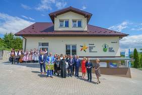 Pokaż zdjęcie: Uczestnicy uroczystego otwarcia siedziby WTZ w Gostwicy. Za uczestnikami widoczny jest wyremontowany budynek.