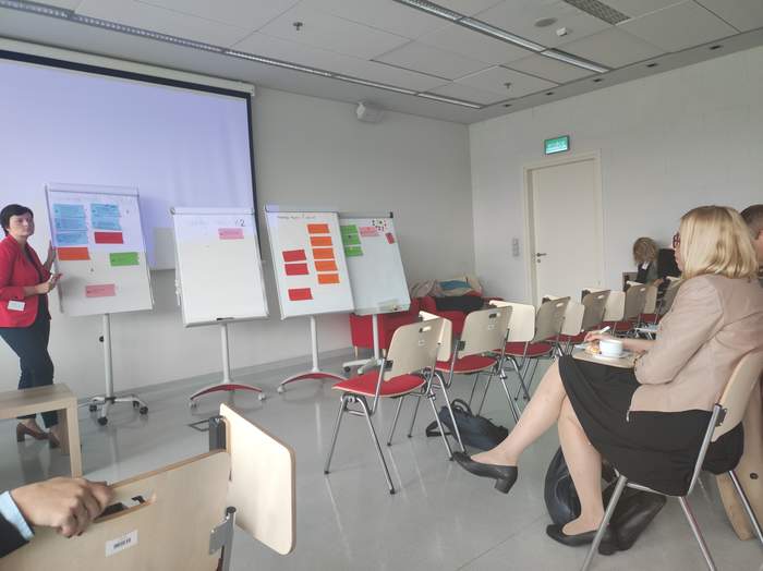 Ludzie siedzący na sali, na przeciwko nich kobiet a prowadząca wykład