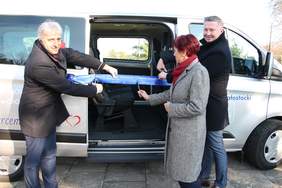 Pokaż zdjęcie: przed busem stoją dwaj mężczyźni po miedzy nimi kobieta w dłoniach trzymają nożyce, którymi przecinają wstęgę.