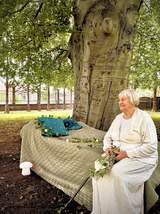 Fotografia przedstawiająca kobietę w bieli siedzącą na ławce w parku i patrzącą w dal