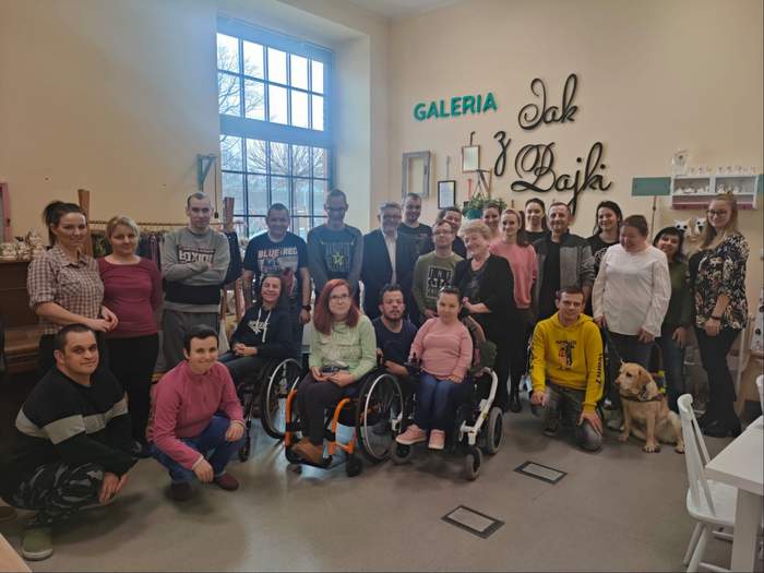 Grupa podopiecznych Zakładu Aktywności Zawodowej w Kluczborku pozujących do zdjęcia z P. Łukaszem Żmudą - Dyrektorem Opolskiego Oddziału PFRON