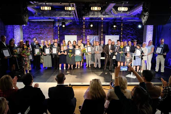 Pokaż zdjęcie: Na scenie stoi duża liczba osób, pozują do pamiątkowego zdjęcia trzymając w ręku dyplomy.