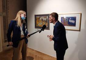 Pokaż zdjęcie: Laureat konkursu udziela wywiadu. Stoi na tle prac