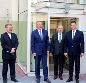 Czterej mężczyźni stoją przed szybem windy, dobudowanej do budynku administracji publicznej. Na zdjęciu są pan Łukasz Żmuda – Dyrektor Opolskiego Oddziału PFRON, pan Roland Fabianek – Starosta Oleski, pan Stanisław Belka – Wicestarosta ora
