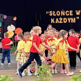 Pokaż zdjęcie: Na scenie tańczą dzieci ubrane w żółte i czerwone koszulki.