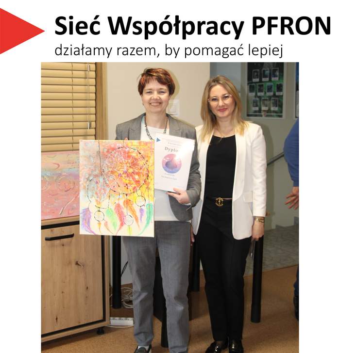 Pokaż zdjęcie: Dwie kobiety w pomieszczeniu. Kobieta z lewej trzyma swoją pracę plastyczną oraz dyplom konkursu „Sztuka Osób Niepełnosprawnych”. W lewym górnym rogu napis: „Sieć Współpracy PFRON – działamy razem, by pomagać lepiej”.