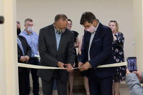 na pierwszym planie 2 mężczyzn przecina rozciągniętą wstęgę, za nimi stoi kilka osób