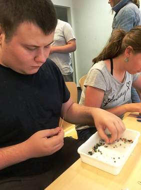 Pokaż zdjęcie: Dwóch uczestników zajęć nawleka koraliki na igły