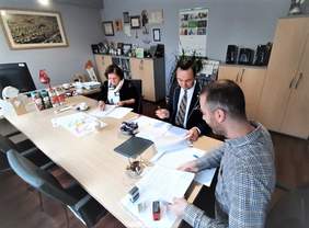 Pokaż zdjęcie: Przy stole, w siedzibie PFRON siedzą od prawej: Dyrektor Kujawsko-Pomorskiego Oddziału PFRON Aleksandra Gierej, Dyrektor Instytutu Ekonomii WSG w Bydgoszczy - dziekan ds. analiz strategicznych Mariusz Barczak oraz Prezes zarządu firmy 4ES Non Profit sp. z o.o. Przemysław Kamycki i podpisuja umowę, na stole leżą dokumenty, stoją filiżanki i miska z cukierkami