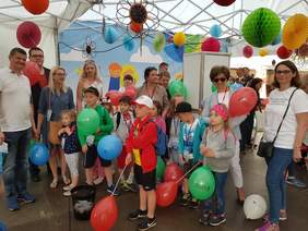 Wnętrze piknikowego namiotu. Grupa osób, wśród nich dzieci z balonami. 