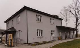 Pokaż zdjęcie: Szary duży dwukondygnacyjny budynek wyposażony w dwa wejścia przystosowane dla osób w z niepełnosprawnościami