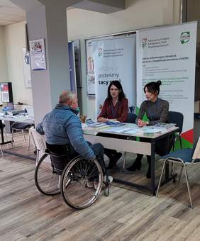Pokaż zdjęcie: dwie kobiety udzielają porad mężczyźnie na wózku.