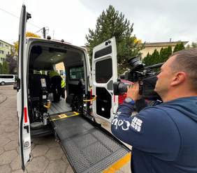 Pokaż zdjęcie: Wnętrze samochodu przystosowanego do przewozu osób z niepełnosprawnością nagrywa operator, który trzyma kamerę. W środku auta stoją mężczyźni. 