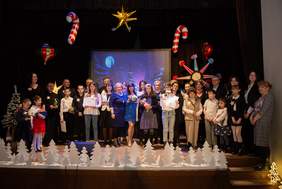 Pokaż zdjęcie: Scena, na scenie wszyscy uczestnicy Kolędowej Szansy na Sukces - dzieci, młodzież dorośli. Dookoła widać dekoracje świąteczne: choinki, gwiazdy.