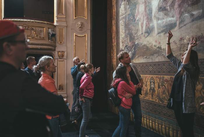 Pokaż zdjęcie: Grupa osób stoi na scenie teatru i przypatruje się kobiecie która gestykuluje rękami.