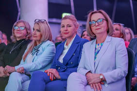 Pokaż zdjęcie: Zdjęcie czterech kobiet siedzących w pierwszym rzędzie podczas konferencji. Kobiety ubrane są w garnitury.