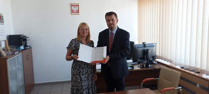 Pokaż zdjęcie: Mężczyzna i kobieta stoją obok siebie w pomieszczeniu, oboje trzymają w rękach umowę