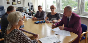 osoby przy podpisaniu umowy siedzące po dwóch stronach stołu, z lewej strony kobieta i mężczyzna, z prawej mężczyzna, kobieta i mężczyzna