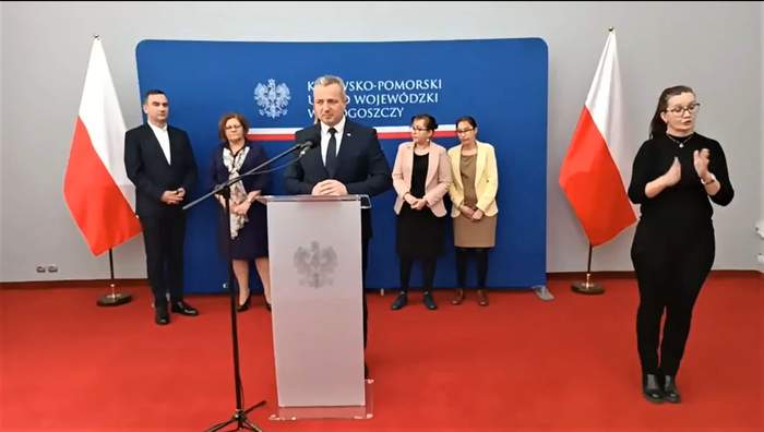 Wojewoda Kujawsko-Pomorski – Mikołaj Bogdanowicz, podczas konferencji prasowej przy mównicy, obok tłumacz języka migowego