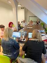 Przy stole siedzą uczestnicy spotkania oraz przy komputerach pracownicy CIDON