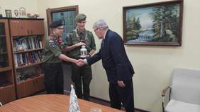 Pokaż zdjęcie: Dwóch harcerzy odwiedziło gabinet dyrektora Łódzkiego Oddziału PFRON. Jeden z harcerzy podaje rękę dyrektorowi, a drugi trzyma w dłoniach Betlejemskie Światło Pokoju. W tle widać obraz na ścianie i regał z książkami. 