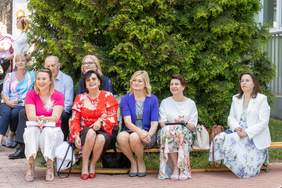 Pokaż zdjęcie: Na ławce siedzi pięć kobiet za nimi rosną tuje.