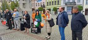 Na rynku w Wąbrzeźnie, w rzędzie stoją kobiety i mężczyźni i spoglądają na uczestnikó Marszu, zgromadzonych przed nimi